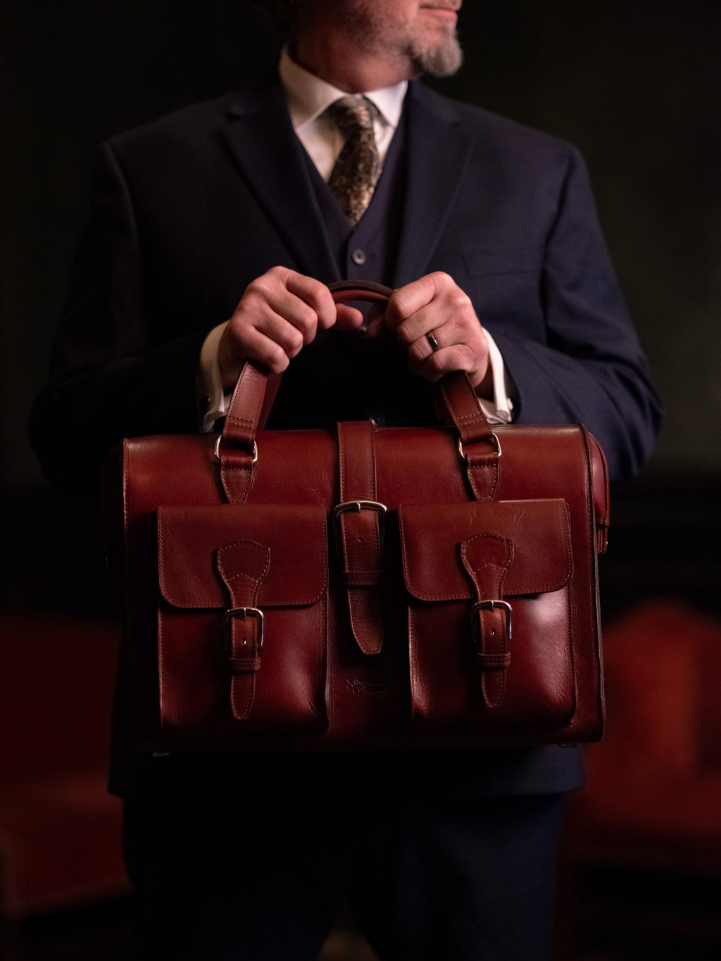 Blackstone Barrister Briefcase in Oxblood held in front of a man wearing a three-piece suit and tie