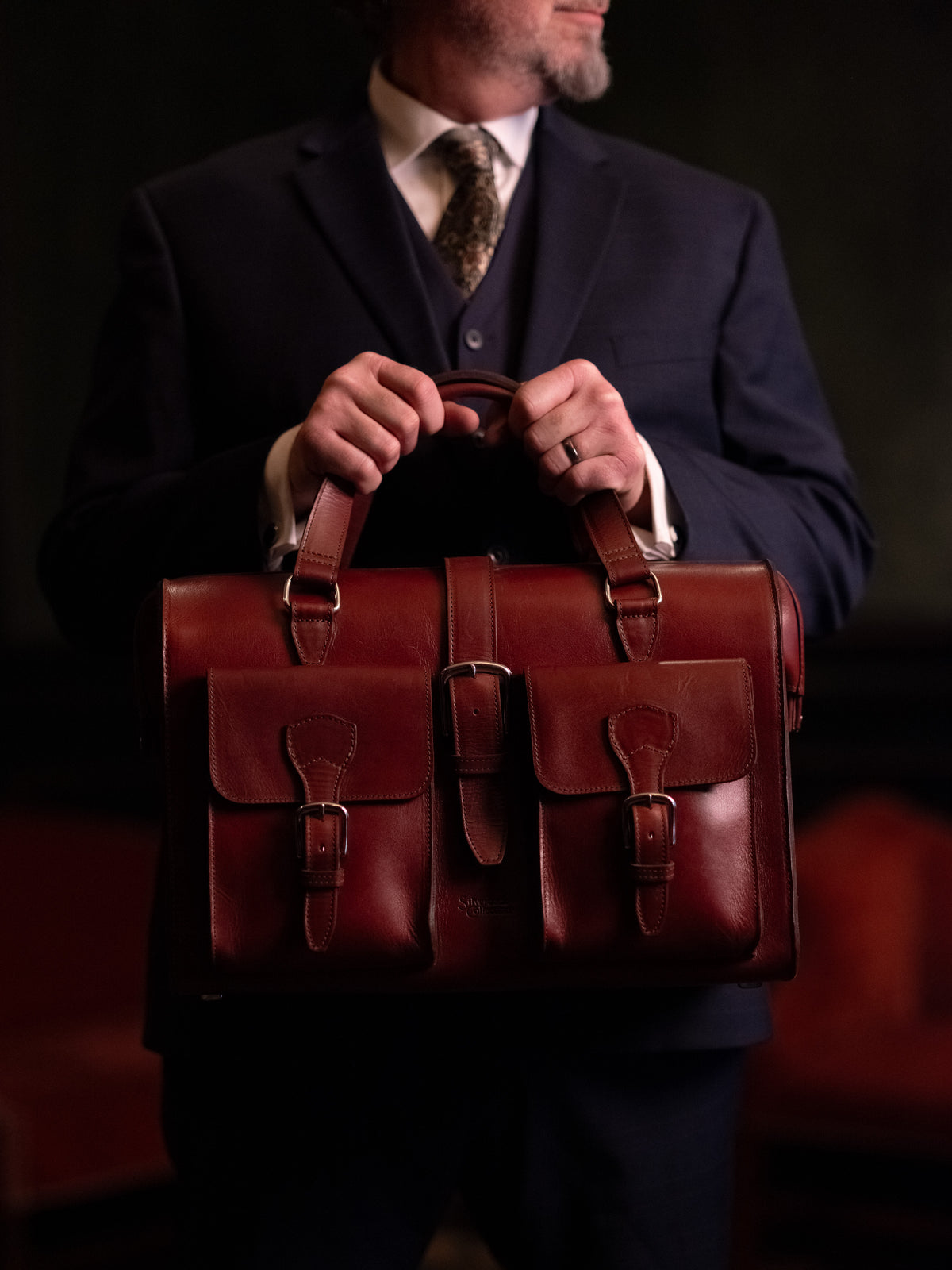 Blackstone Barrister Briefcase in Oxblood held in front of a man wearing a three-piece suit and tie