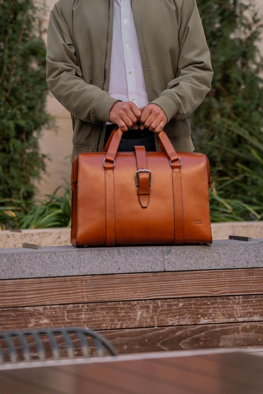 Spurgeon Briefcase in English Tan held by its handles in front of a man in a green jacket outdoors
