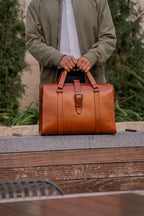 Spurgeon Briefcase in English Tan held by its handles in front of a man in a green jacket outdoors