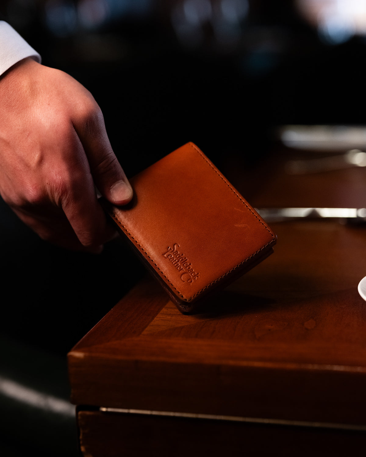 William Penn Bifold Wallet in English Tan being picked up from a dark wooden table by hand