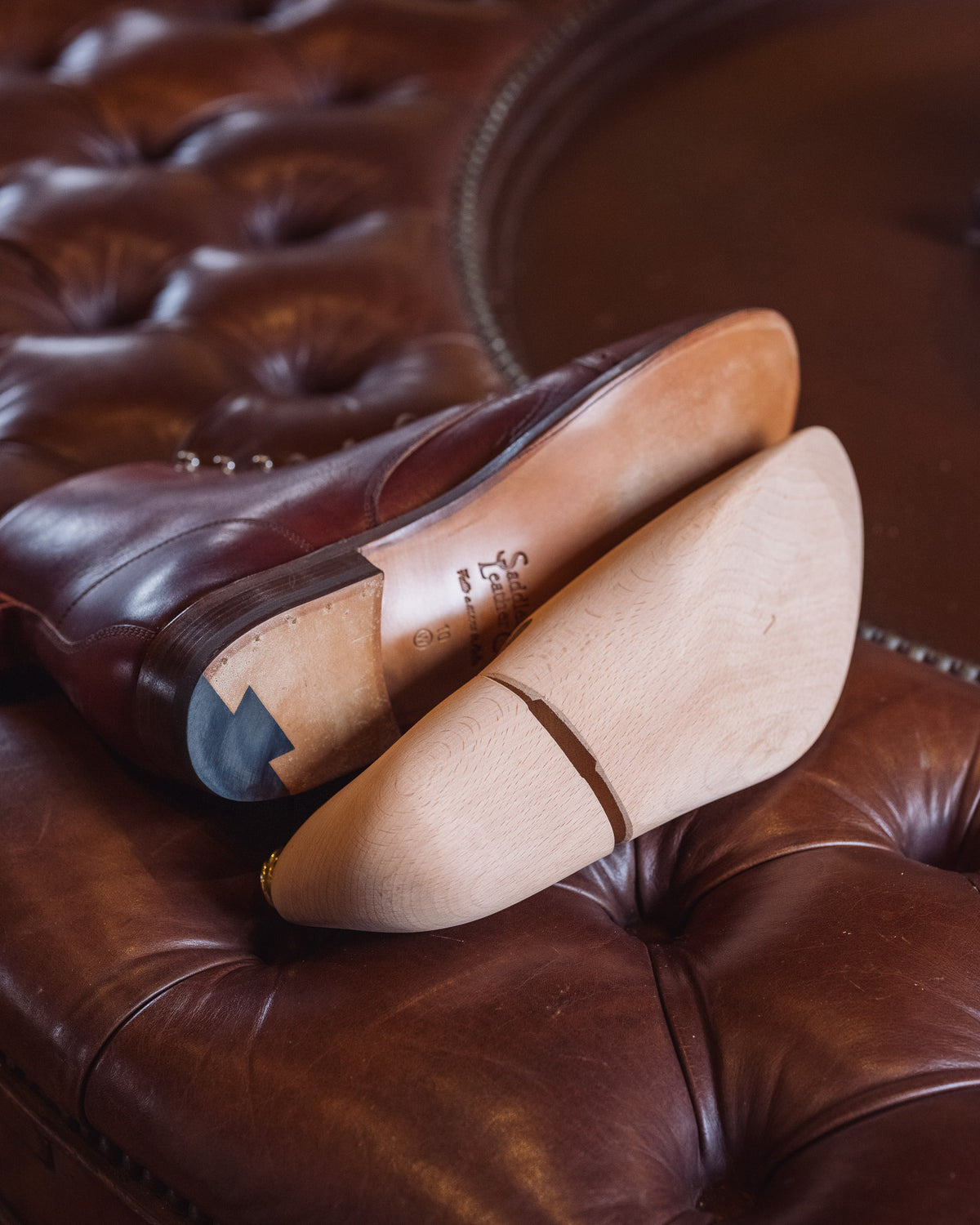 Shoe Tree laid against the leather sole of a brown boot on a tufted leather ottoman