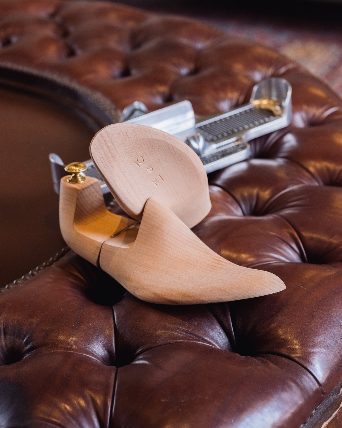 Shoe Tree pair stacked on a foot measuring device atop a tufted leather ottoman