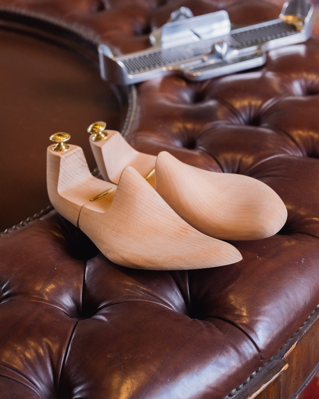Shoe Tree pair resting on a tufted leather ottoman beside a foot measuring device