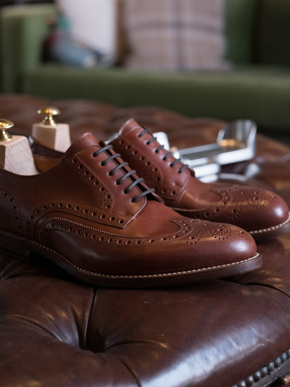 Shoe Tree pair fitted in brown wingtip shoes on a tufted leather ottoman
