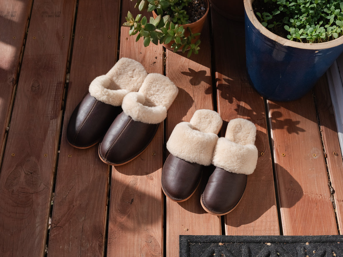 Women's Sheepskin Slippers in Dark Coffee Brown, two pairs on a sunny wooden deck by potted plants