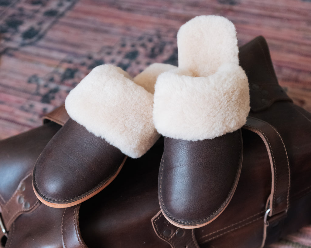 Women's Sheepskin Slippers in Dark Coffee Brown, front view of pair resting on a leather bag