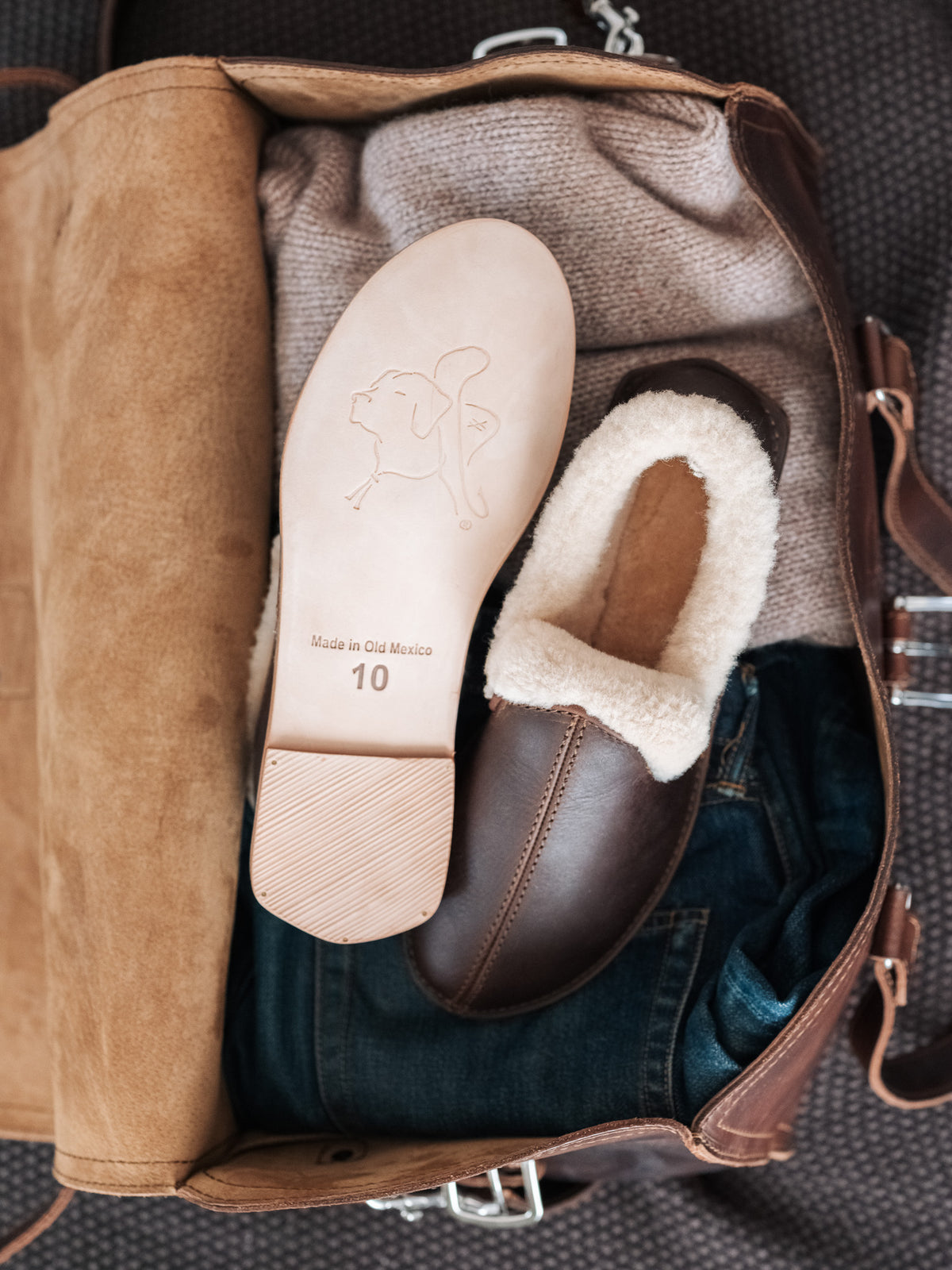 Sheepskin Moccasins in Dark Coffee Brown in an open leather bag, one flipped to show the leather sole with size stamp