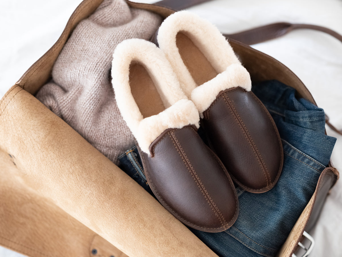 Pair of Sheepskin Moccasins in Dark Coffee Brown, top view on jeans and a sweater in an open leather bag