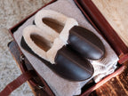 Pair of Sheepskin Moccasins in Dark Coffee Brown, top view on a folded sweater in an open leather case