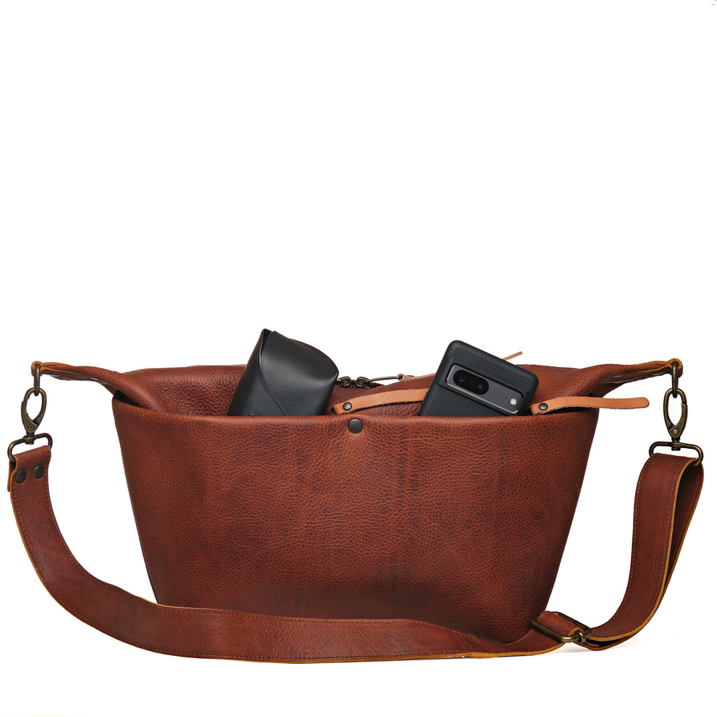 London Sling Large in Chestnut, front view with a phone and glasses case peeking from the open top