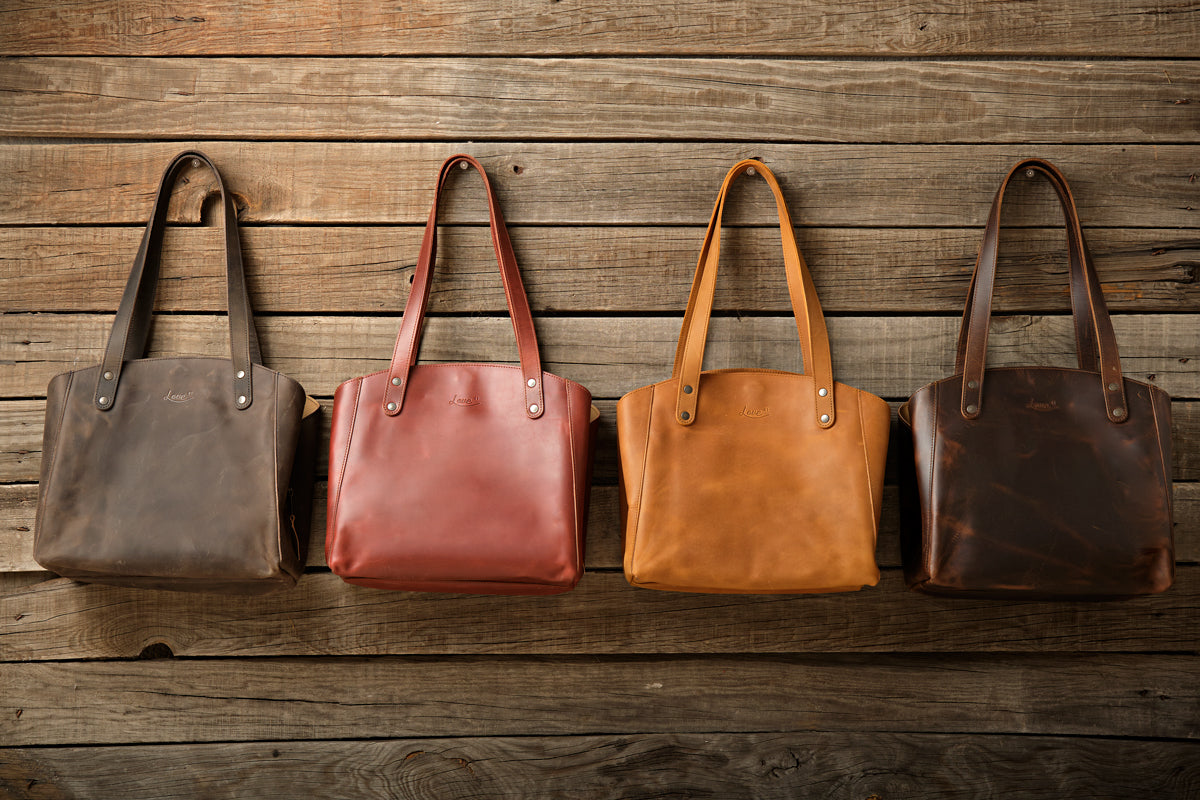 Leather Organizer Satchel in Black, Chestnut, Tobacco and Dark Coffee Brown hanging side by side on a wood wall