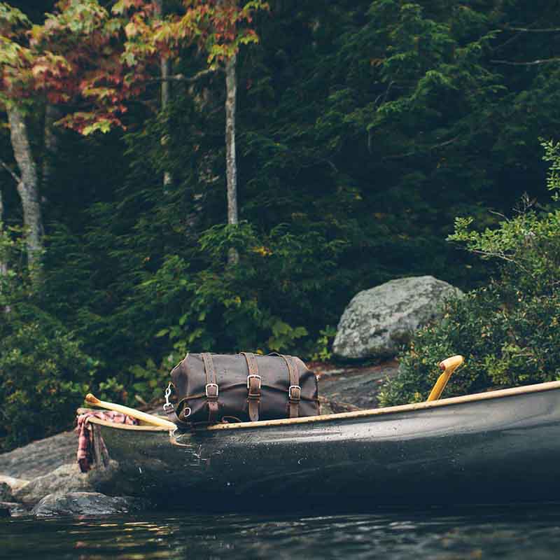 20" Waterbag in Dark Coffee Brown, resting in a canoe on a forest lake shore