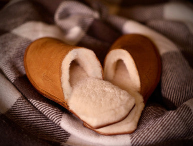 Pair of Women's Sheepskin Slippers in Tobacco on a plaid blanket, close-up of the fleece lining