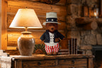 2026 Uncle Sam Teddy Bear on a rustic wooden chest beside a lit lamp and old books in a log cabin room