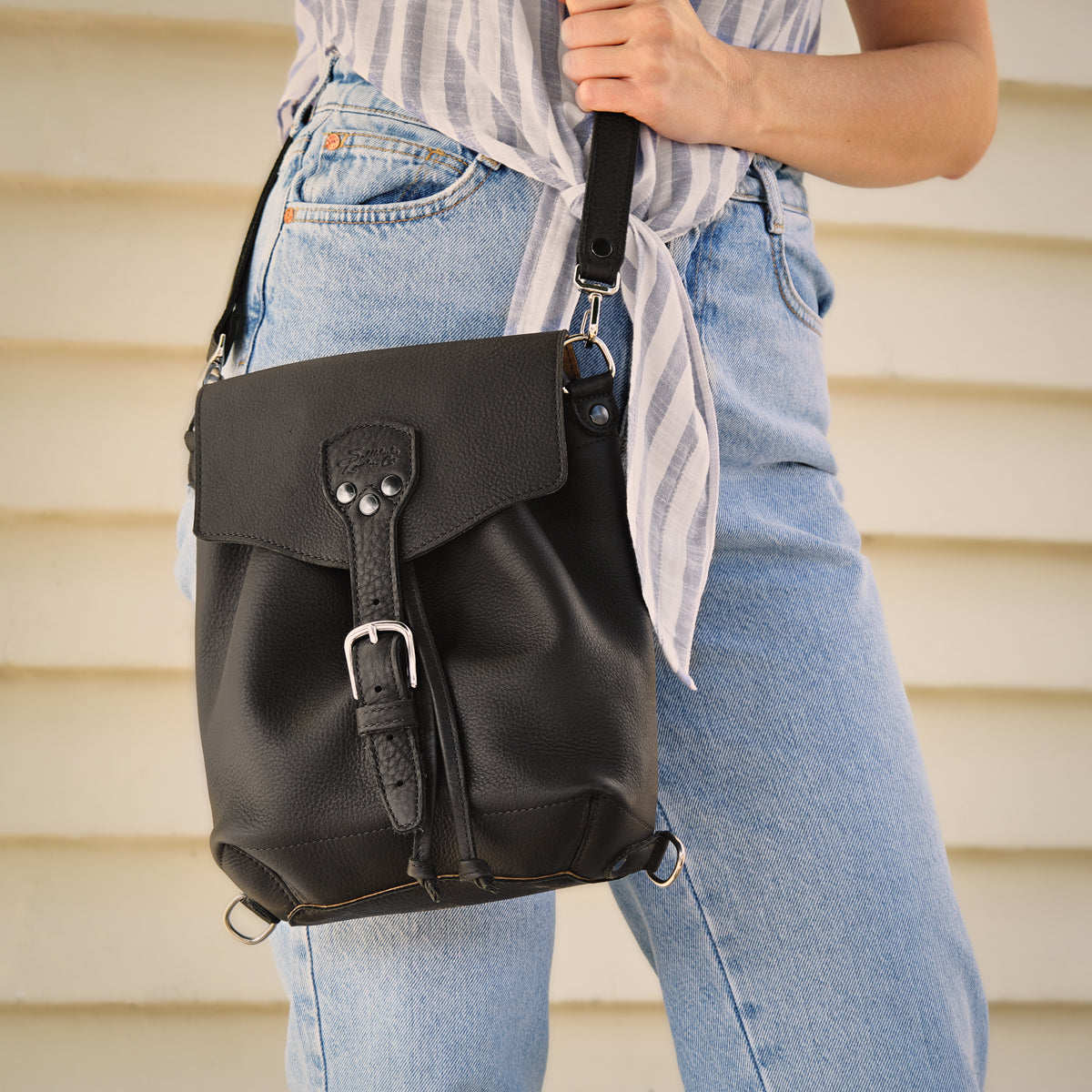 10" Convertible Crossbody in Black, front view held by its strap by a woman in jeans