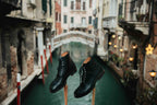 Pair of high quality black leather Officer Boots on wooden stands above a Venice canal, side view