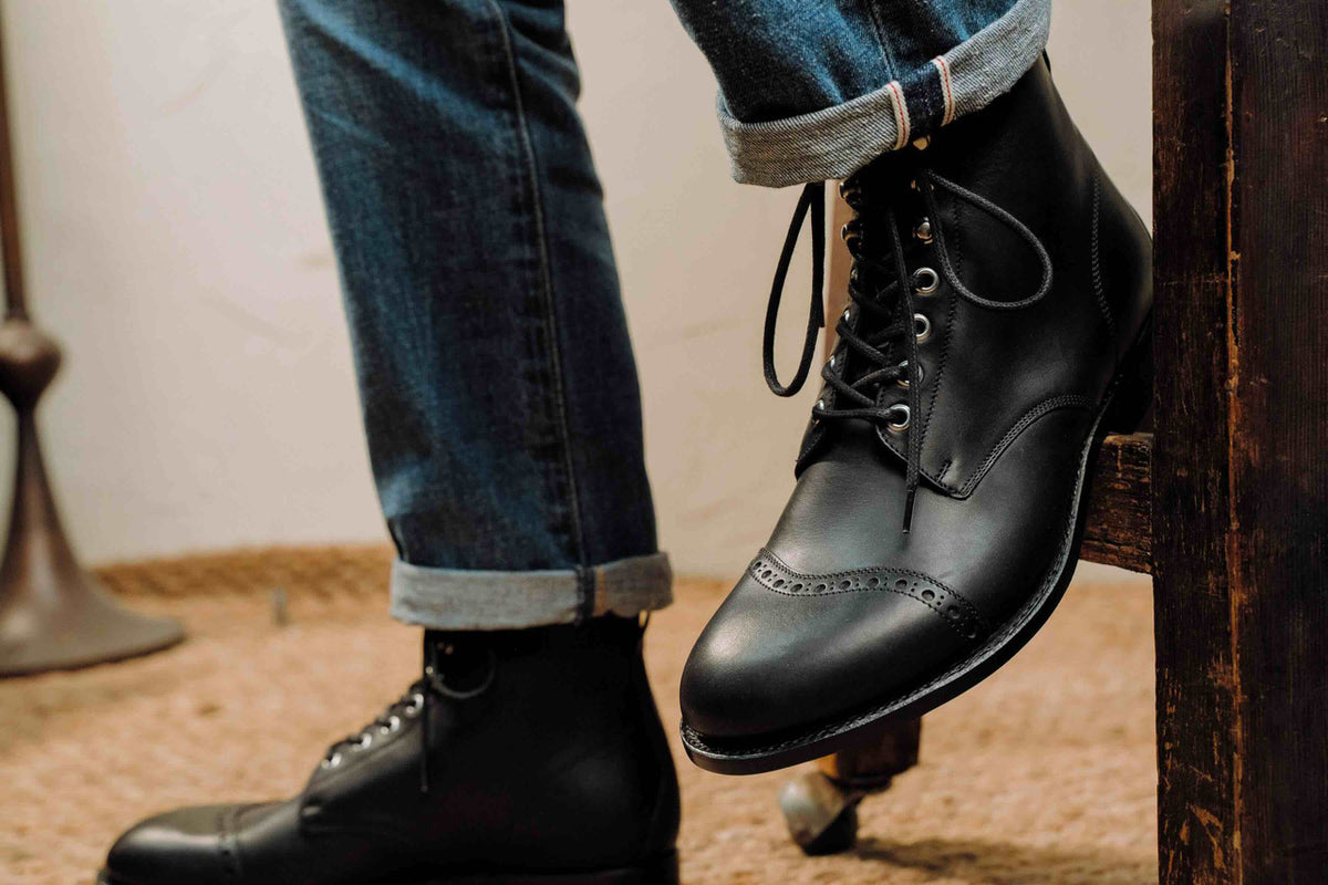 High quality black leather Officer Boot worn with cuffed jeans, foot raised on a wooden step, side view