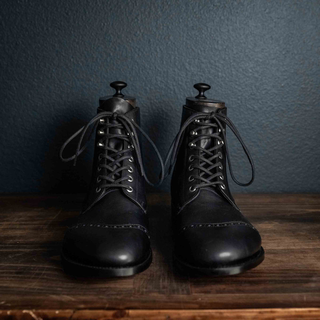 Pair of high quality black leather Officer Boots with shoe trees on a wooden table, front view