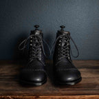 Pair of high quality black leather Officer Boots with shoe trees on a wooden table, front view