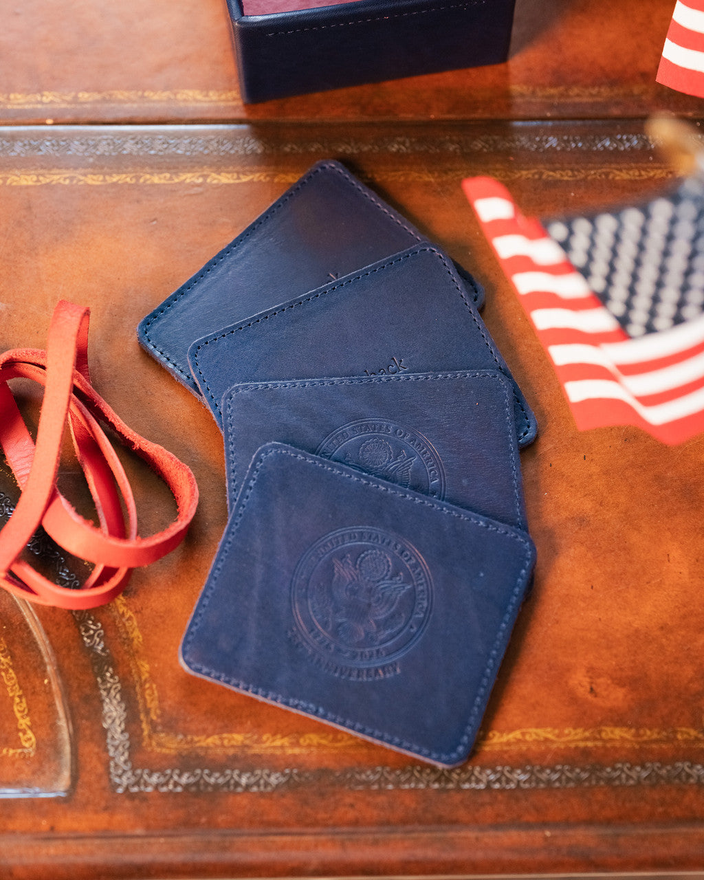 Saddleback Club Membership John Adams Leather Coaster Set in Blue and Red, fanned coasters on a wood desk beside an American flag