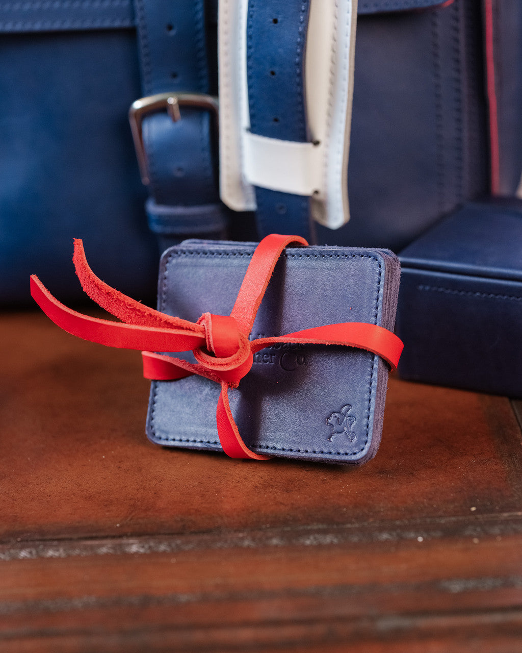 Saddleback Club Membership John Adams Leather Coaster Set in Blue and Red, stacked coasters tied with red strap on a desk
