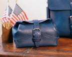 Saddleback Club Membership George Washington Leather Roll-Up Toiletry Bag in Blue on a wood desk with small American flags
