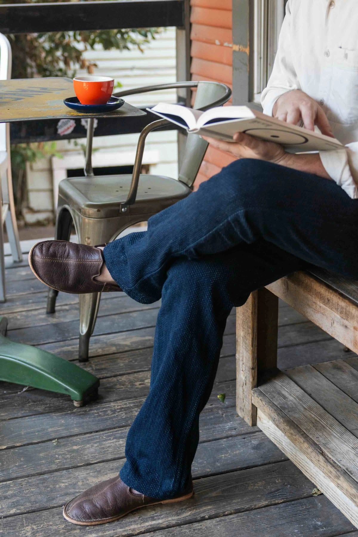 Barefoot Slip-on Shoe in Dark Coffee Brown, worn by a man reading on a cafe porch