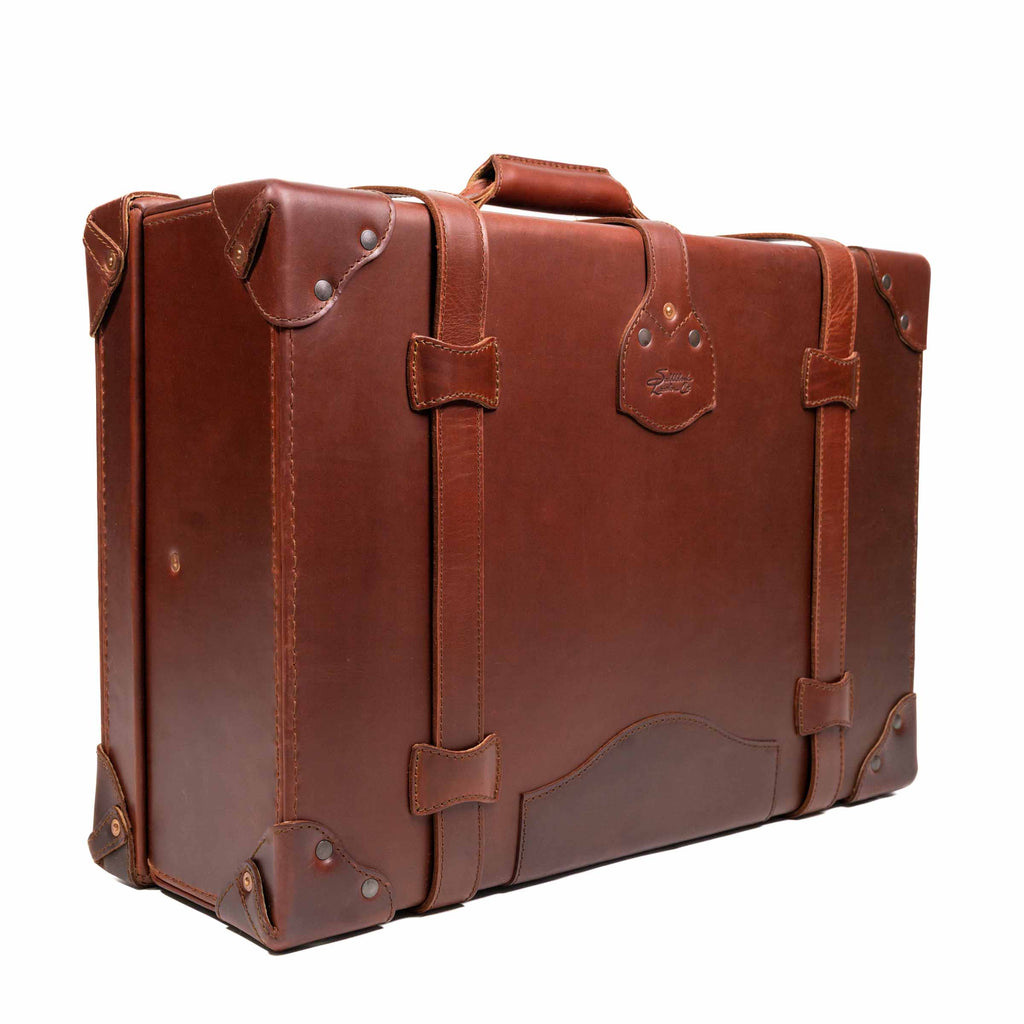 Grandfather Medium Suitcase in Chestnut, angled back view with top handle, straps and riveted corners