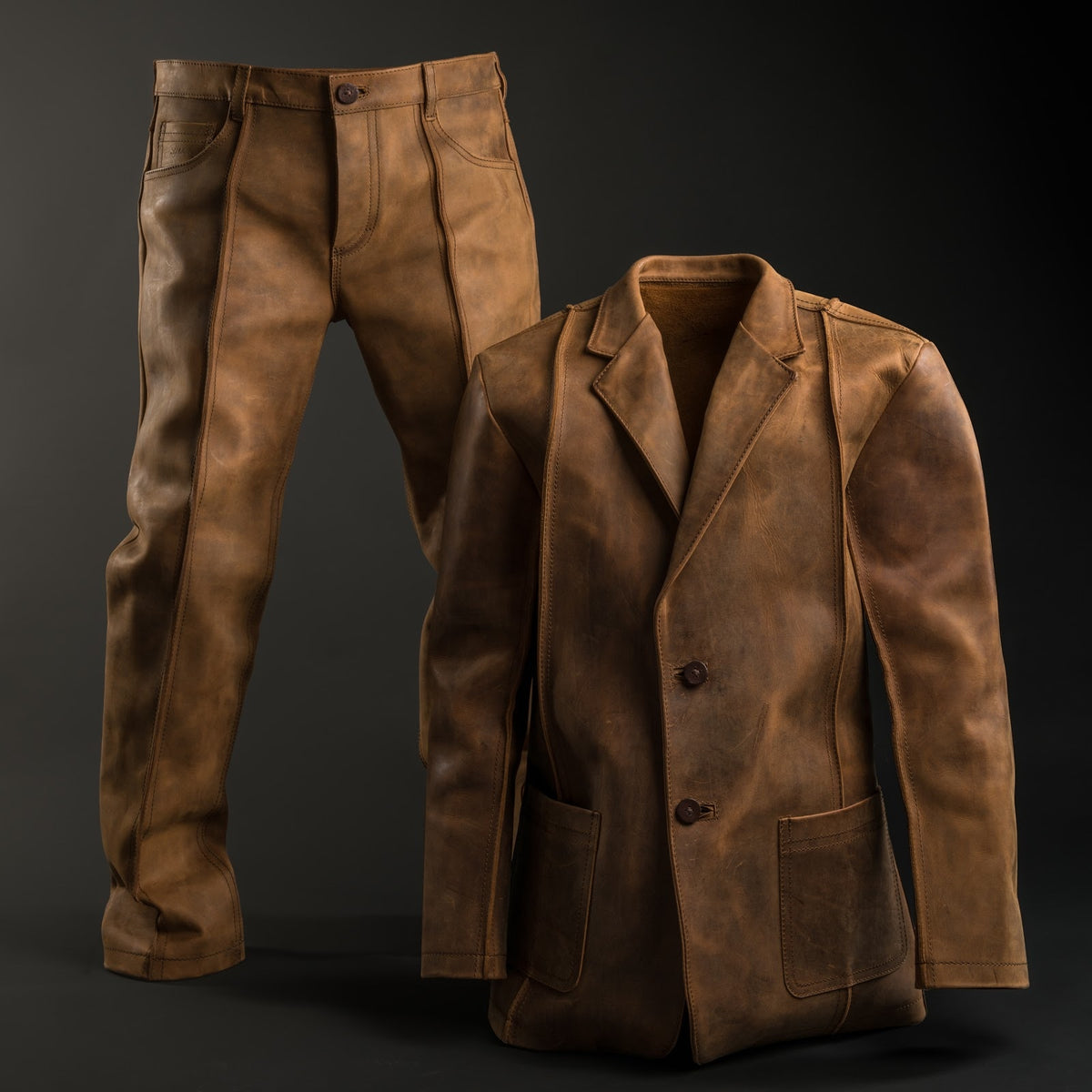 A worn-in tan leather blazer and matching leather jeans, standing upright on their own against a dark backdrop.