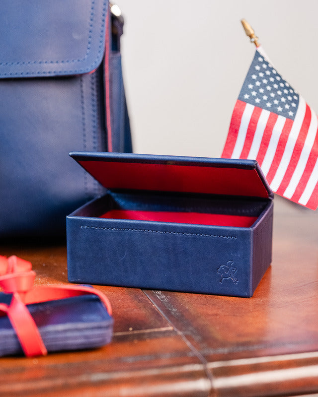 The navy leather cash box standing open to show its red lining, beside a small United States flag