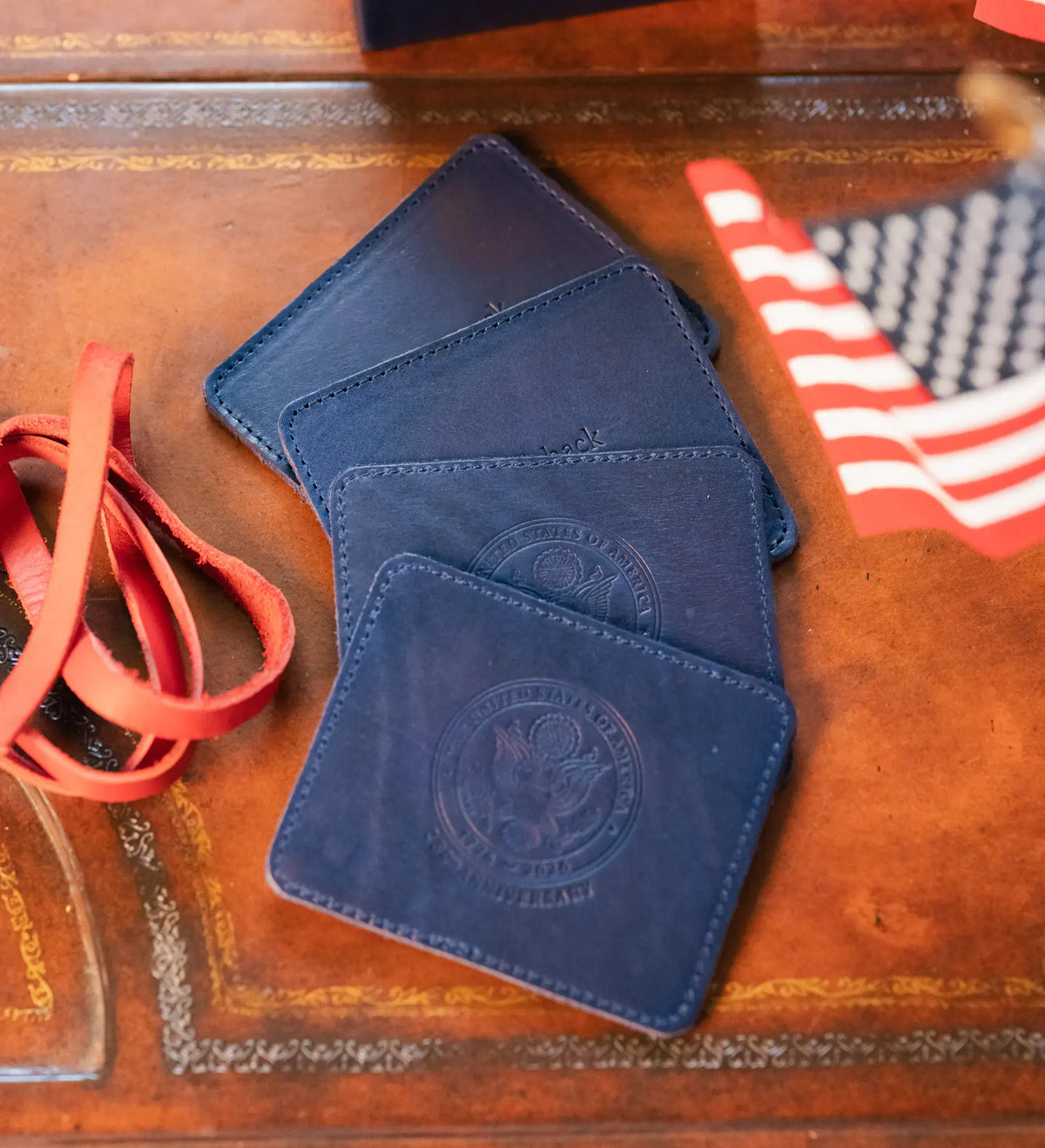 Three embossed navy leather coasters laid out with a red strap and a United States flag on a leather desktop