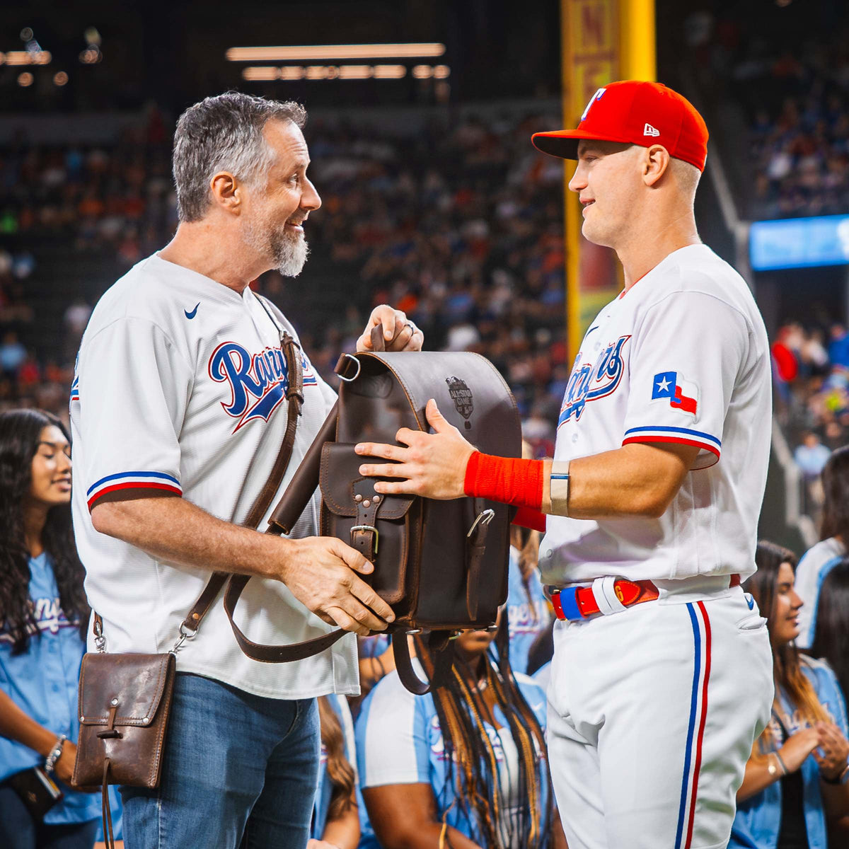 Dave Munson handing Josh Jung a dark brown Tank Leather Backpack on the field, both smiling.