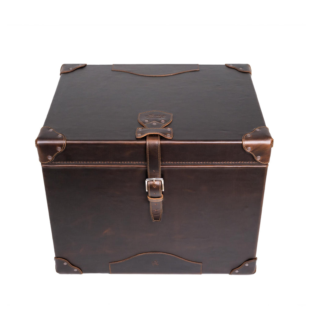 Leather Small Trunk in Dark Coffee Brown, closed front view from above showing lid, embossed logo patch and buckled strap