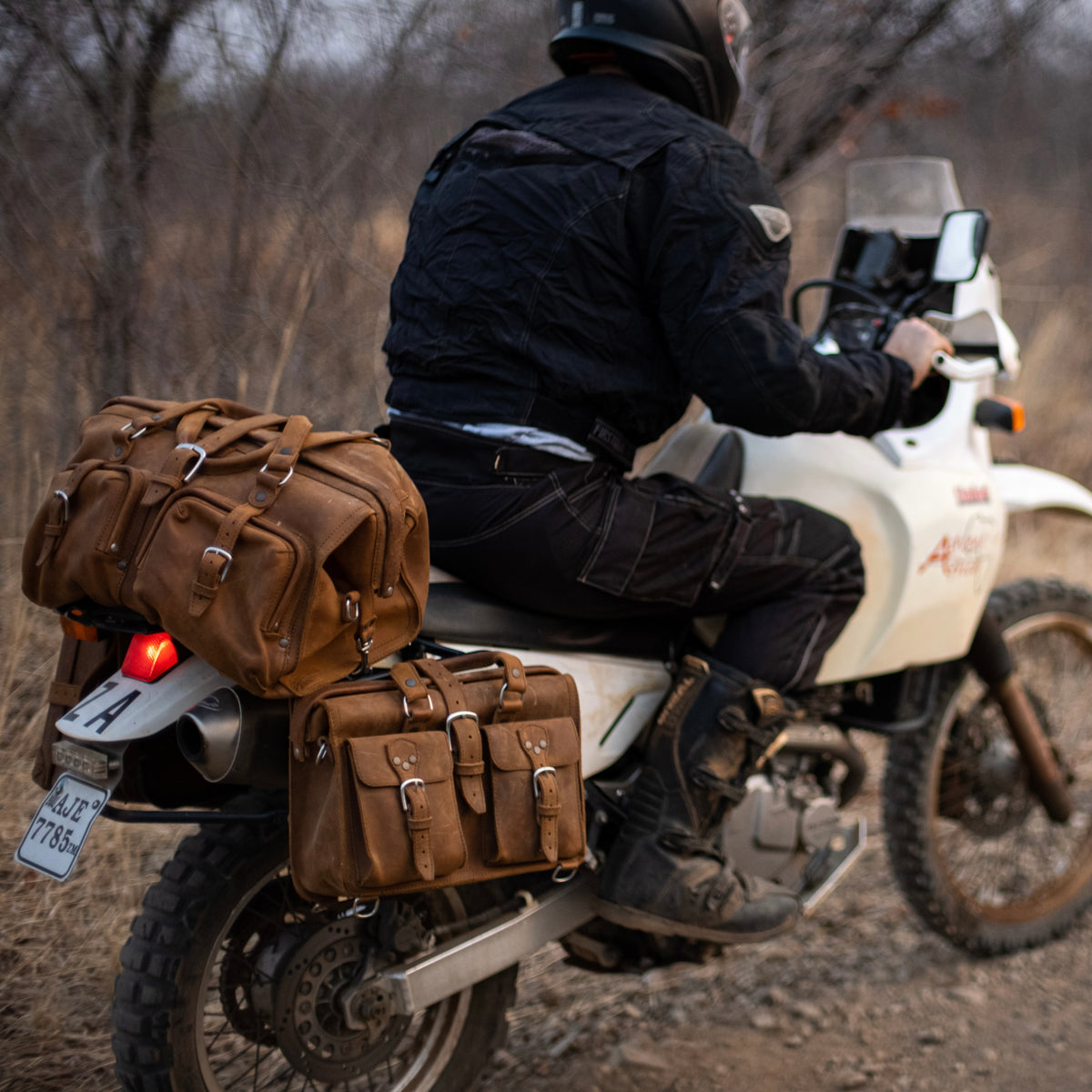 Deep Pocket Leather Duffle Bag in Tobacco strapped to the back of a motorcycle ridden by a man on a dirt trail