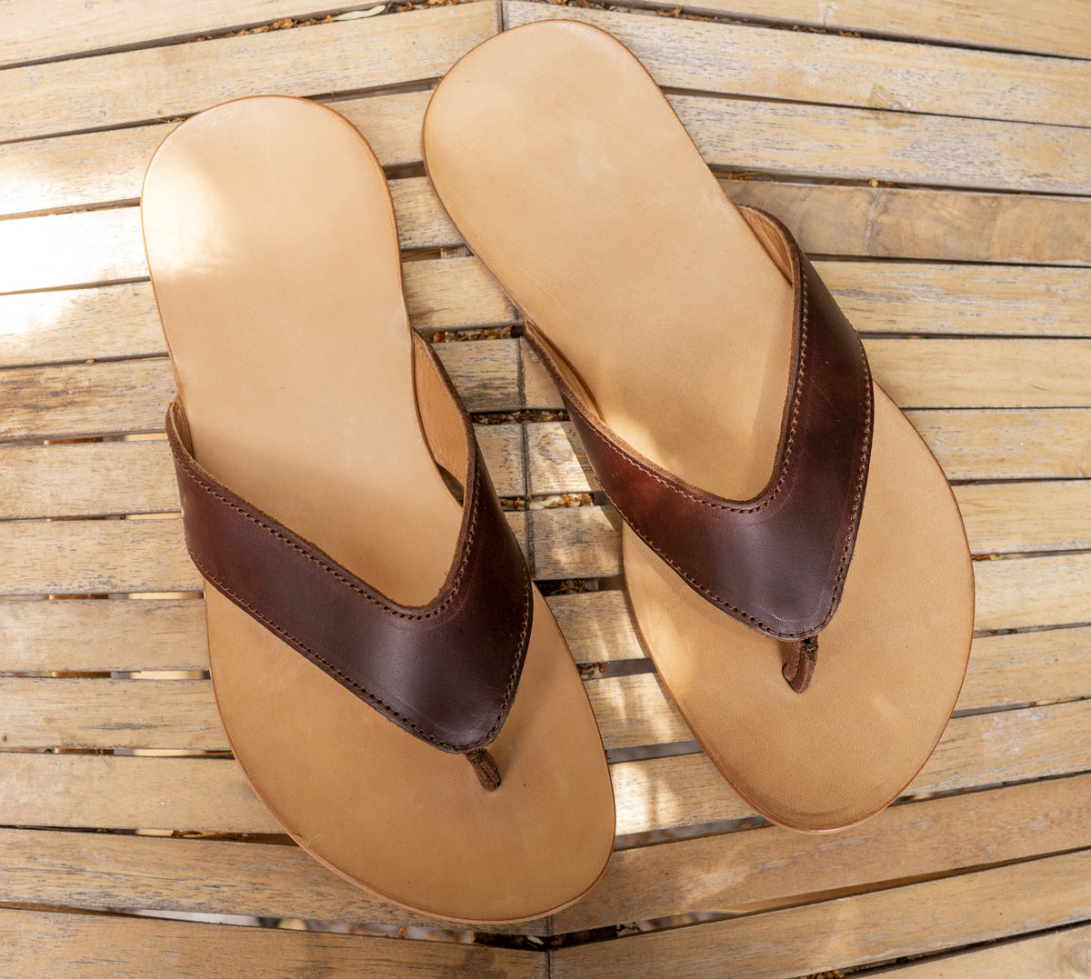 Flip Flops in Chestnut, top view of a pair with untreated natural leather footbeds on a wooden deck