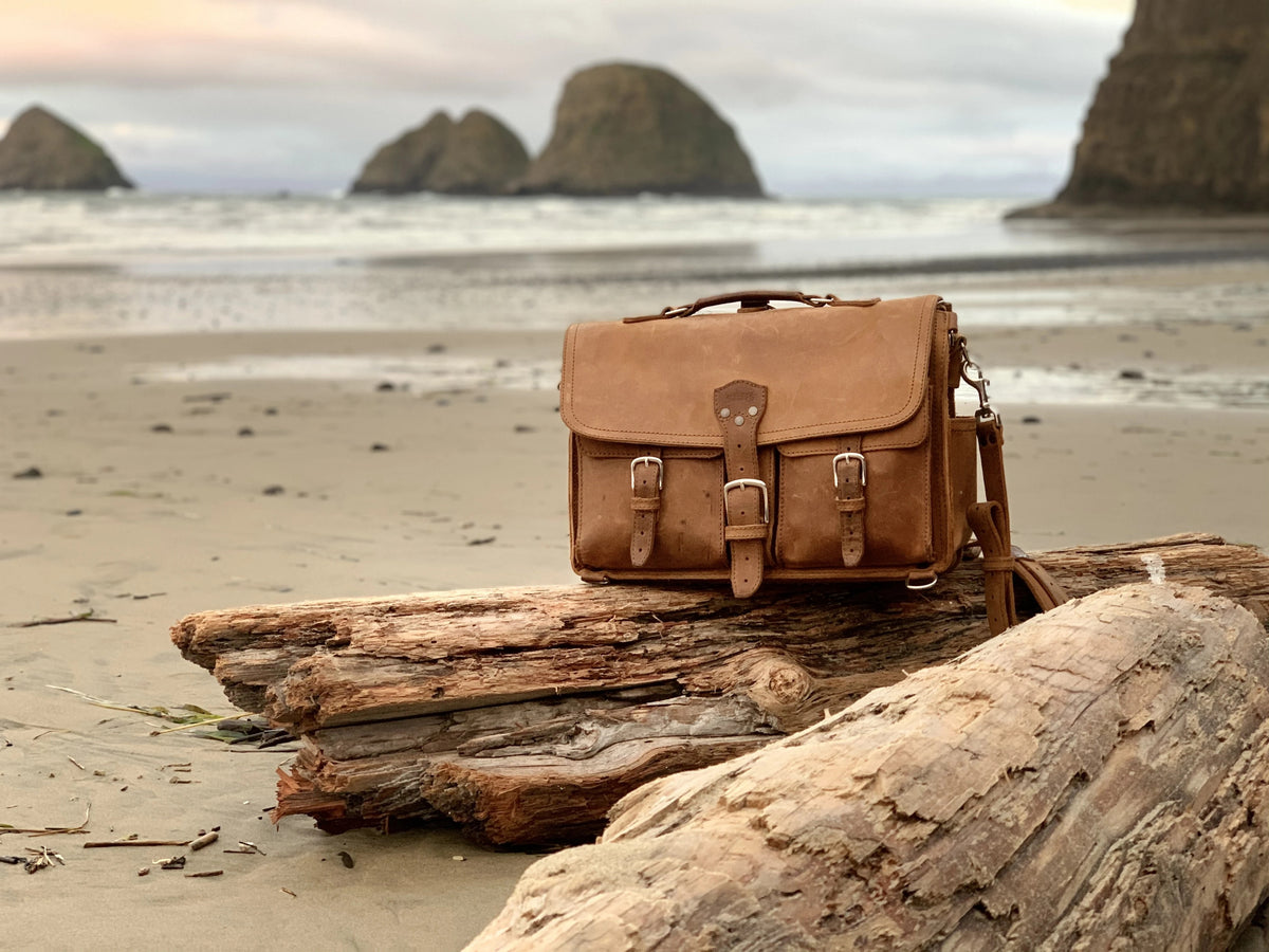 Brown Front Pocket Leather Briefcase on driftwood at a beach with sea stacks behind