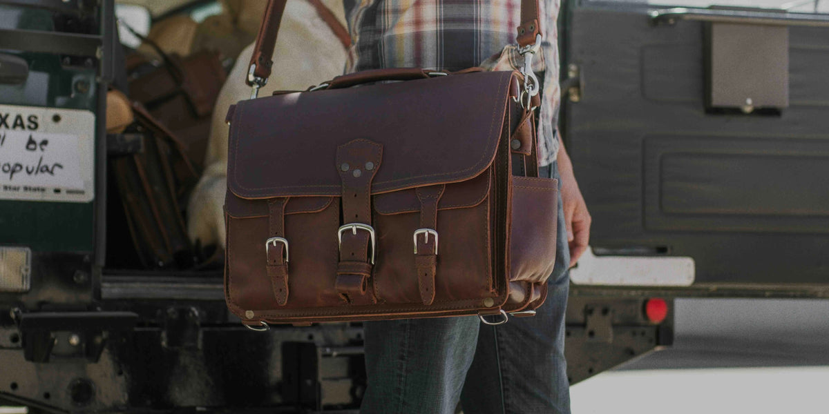 Man carrying a Chestnut Front Pocket Leather Briefcase on its shoulder strap beside a truck