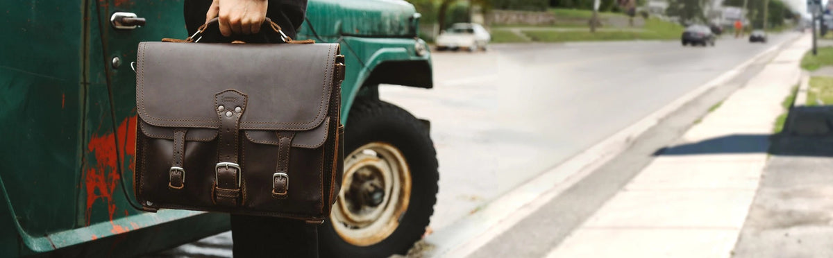 Hand carrying a dark brown Front Pocket Leather Briefcase beside a vintage green truck