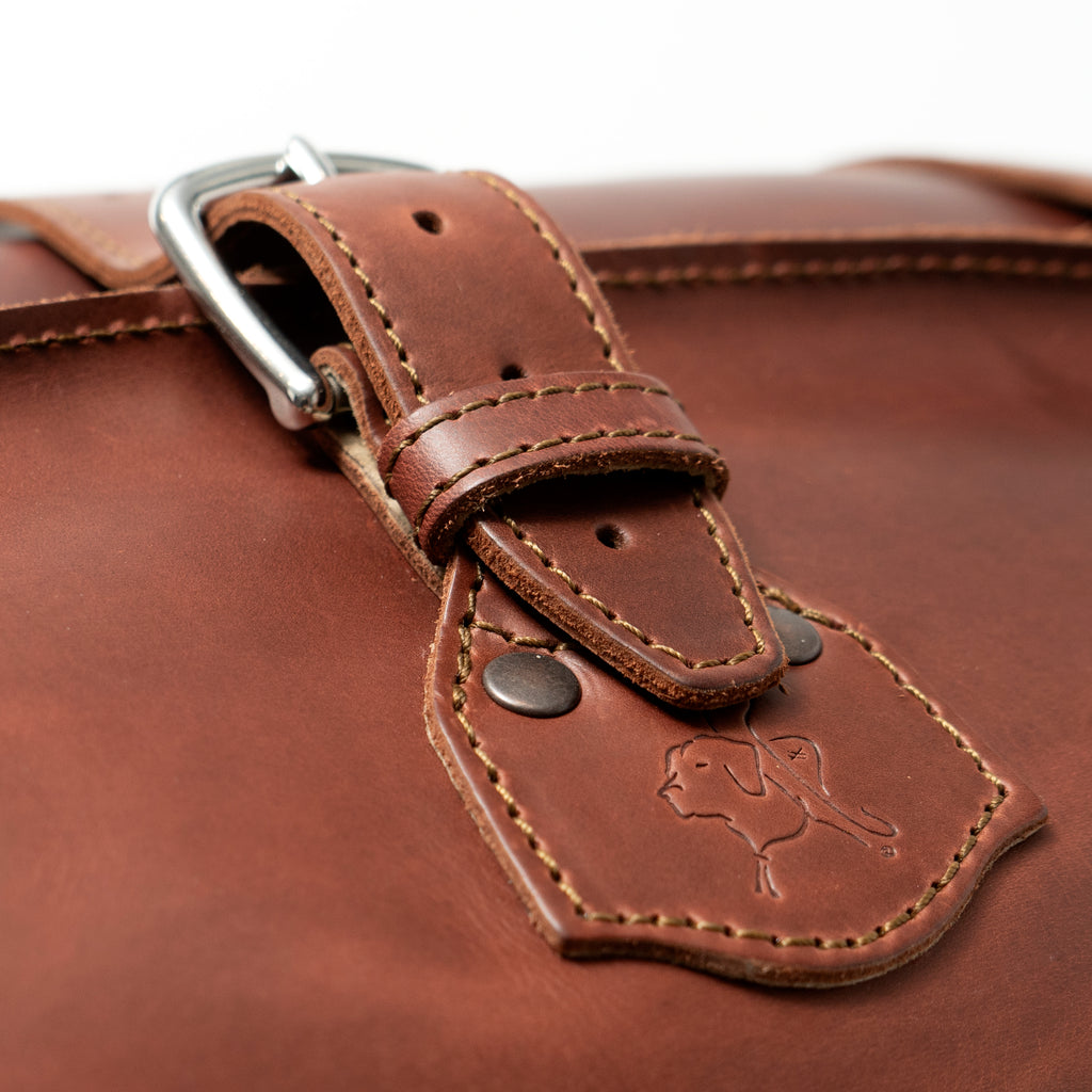 24" Waterbag in reddish brown, close-up of a buckle strap and riveted tab with embossed pig logo