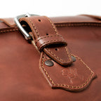 24" Waterbag in reddish brown, close-up of a buckle strap and riveted tab with embossed pig logo