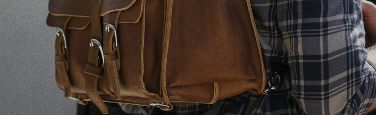 Brown leather bag with buckled front pockets carried beside a plaid shirt