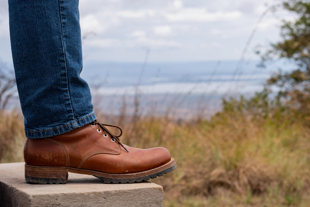 Huntsman Boots in brown leather, side view of boot worn with jeans on a stone ledge outdoors