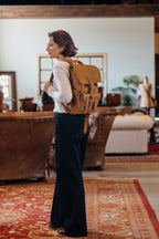 Small Front Pocket Backpack in Tobacco worn by a woman in profile in a rustic room with leather sofas and a red rug
