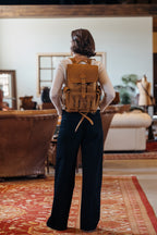 Small Front Pocket Backpack in Tobacco worn by a woman seen from behind in a rustic room with leather sofas and a red rug