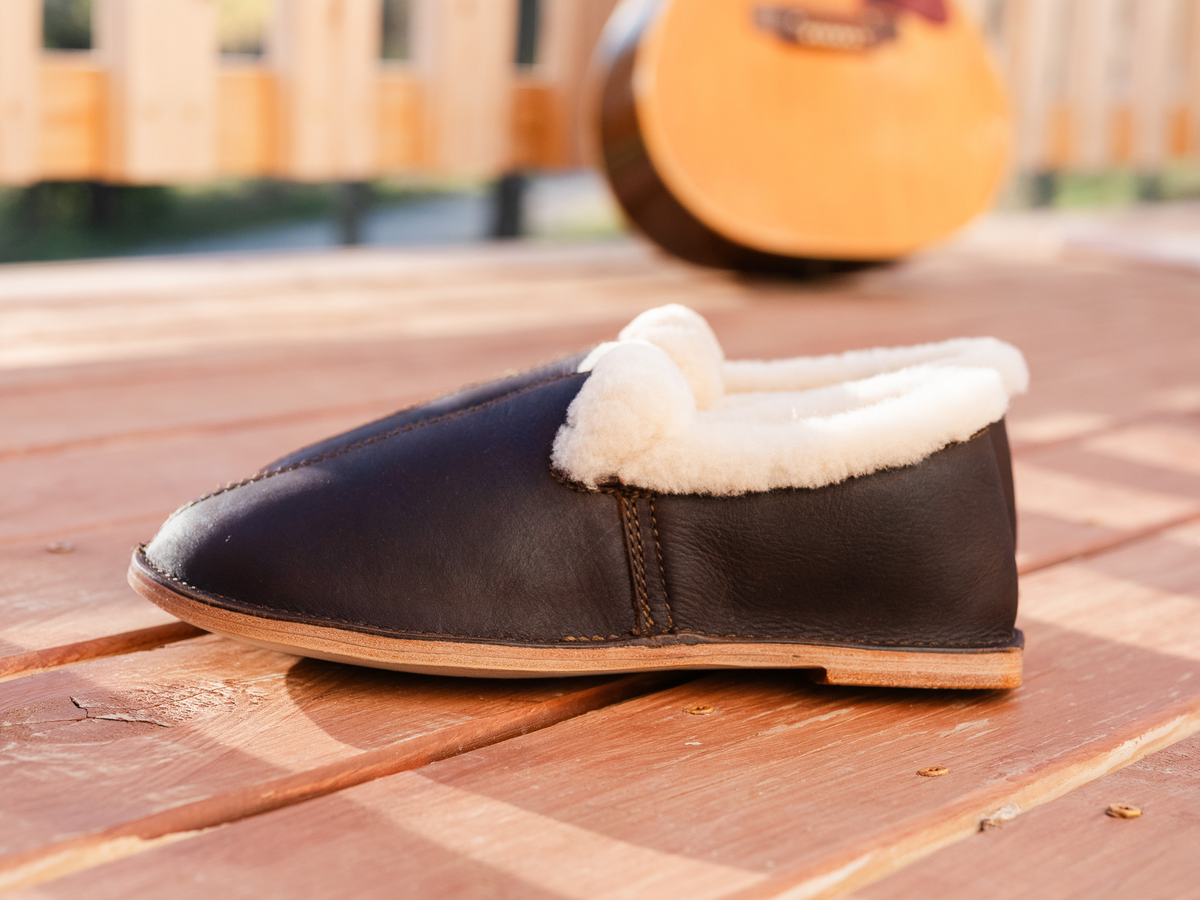 Sheepskin Moccasins - New Design in Dark Coffee Brown, side view on a sunlit wood deck with a guitar behind