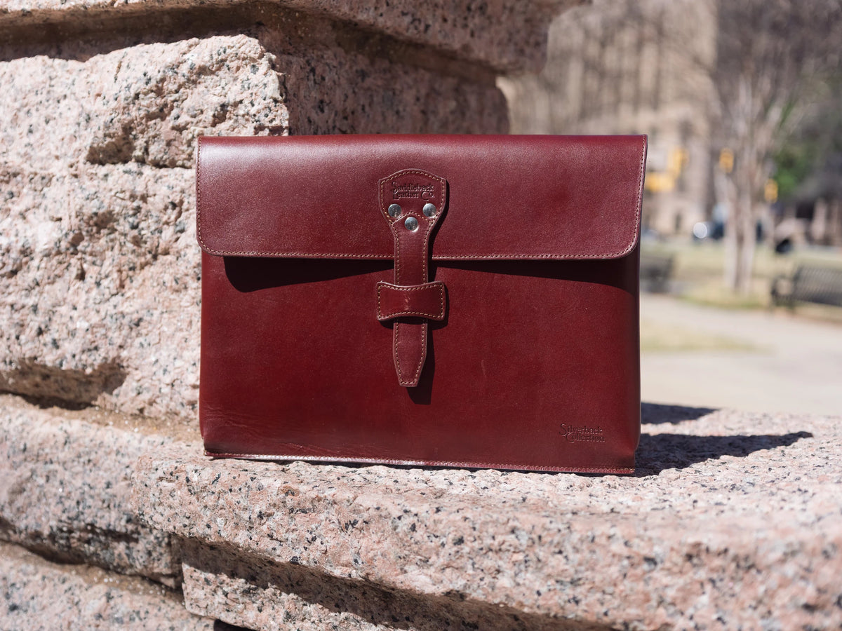 Silverback Document Holder in Oxblood, front view standing on a sunlit granite ledge with strap closure