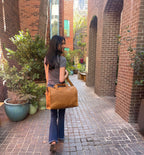Simple Overnight Leather Duffle Bag in Tobacco, carried on the shoulder by a woman walking down a brick alley