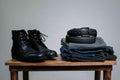 Italian Casual Belt in Pitch Black coiled on folded jeans beside black leather boots on a wooden stool