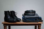 Italian Casual Belt in Pitch Black coiled on folded jeans beside black leather boots on a wooden stool